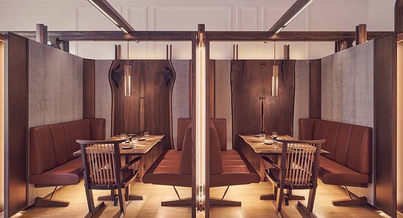 A sophisticated dining space with intimate wooden booths, leather seating, and warm ambient lighting.