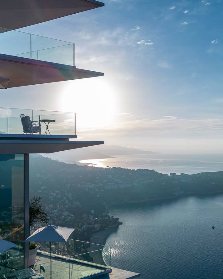 A striking modern building with glass balconies overlooking the coastline, bathed in golden sunlight at sunset.