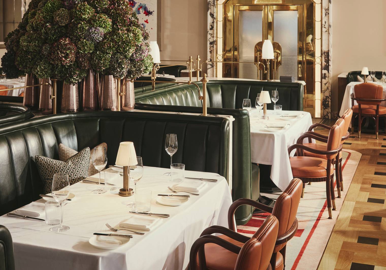 Opulent dining room with green leather banquettes, polished wood chairs, crisp white table linens, and a luxurious art deco ambiance.