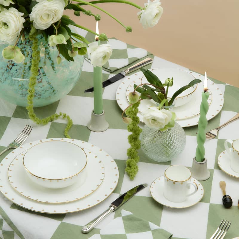 Refined table setting with fine china, green candles, white flowers, and geometric tablecloth in soft tones.