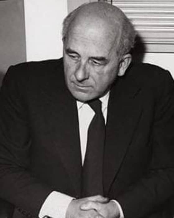 Black-and-white portrait of a thoughtful man in a suit, hands folded, exuding a sense of introspective elegance